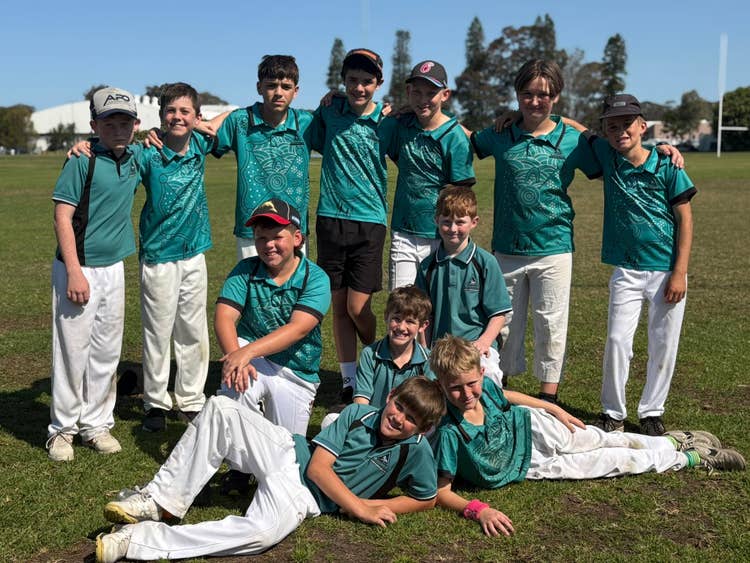 12 boys smiling and hugging and posing with eachother in cricket uniform